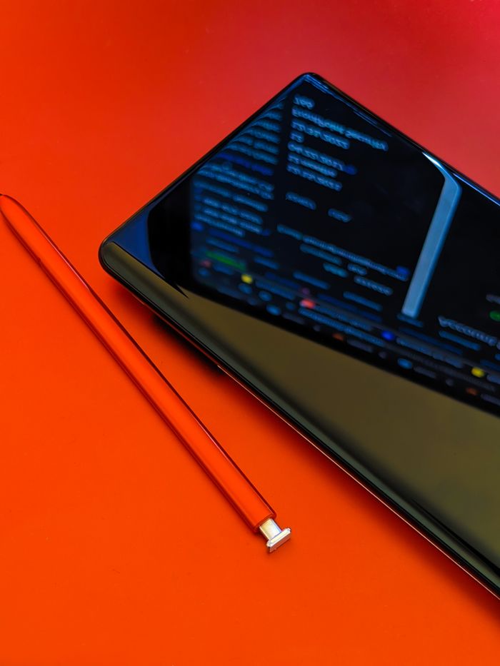 Gros plan sur un smartphone avec un stylet posé sur une surface rouge éclatante, mettant en valeur la technologie moderne.